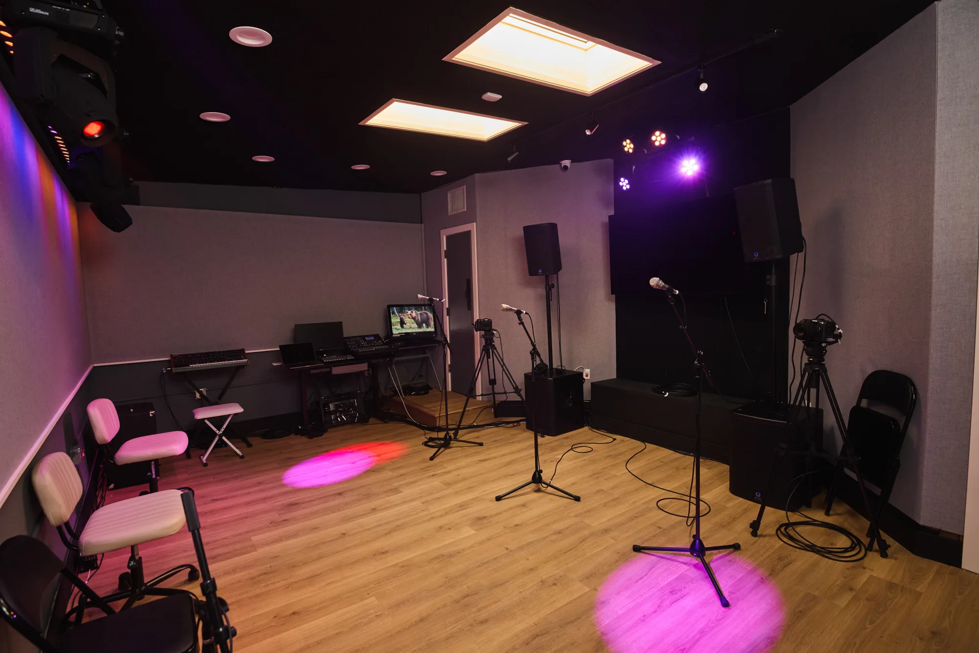 Rehearsal Room 2 as it is today: grey acoustic fabric walls, fluorescent ceiling panels, mic stands, keyboard rig and folding chairs.